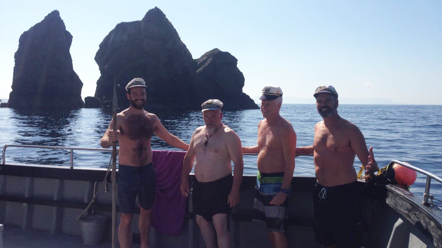 Four men in swimsuits on a boat beside an island