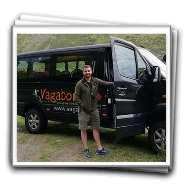 A black small-group tour bus with a tour guide standing in front of vehicle with the door open