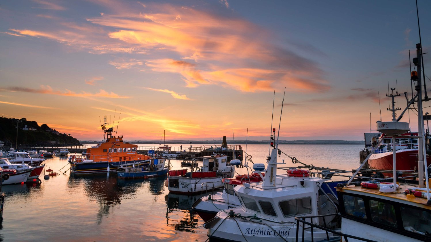 Ballycotton harbour at sunset with boats in the foreground, including a lifeboat