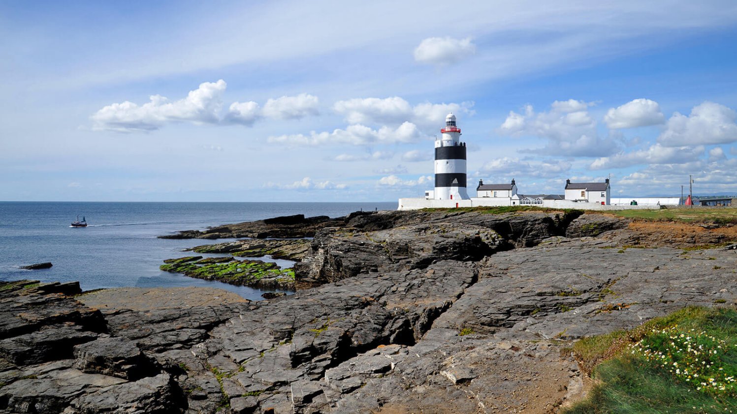 Striped black and white Hook Lighthouse with a rocky shore in the foreground